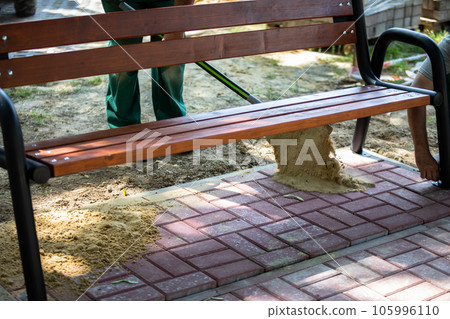 A construction worker backfills freshly laid paving stones with sand. 105996110