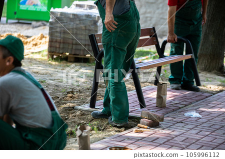 Physical workers set up a park bench at a designated spot in a city park. 105996112