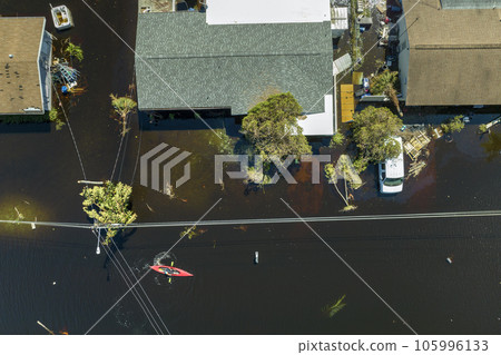 Aftermath of flooding natural disaster. Kayak boat floating on flooded street surrounded by hurricane Ian rainfall flood waters homes in Florida residential area Aftermath of flooding natural disaster. Kayak boat floating on flooded street surrounded by hurricane Ian rainfall flood waters homes in Florida residential area 105996133