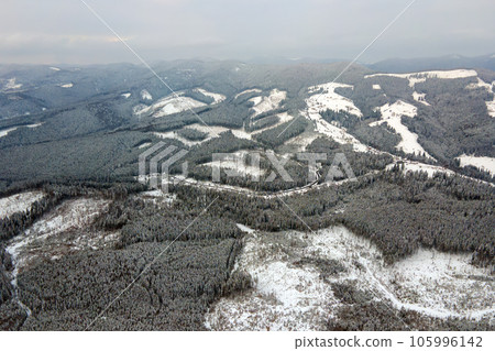 Aerial view of winter landscape with mountain hills covered with evergreen pine forest after heavy snowfall on cold quiet evening. Aerial view of winter landscape with mountain hills covered with evergreen pine forest after heavy snowfall on cold quiet evening. 105996142