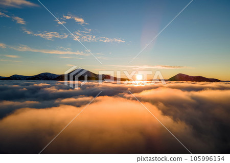 Aerial view of vibrant sunrise over white dense fog with distant dark Carpathian mountains on horizon. 105996154