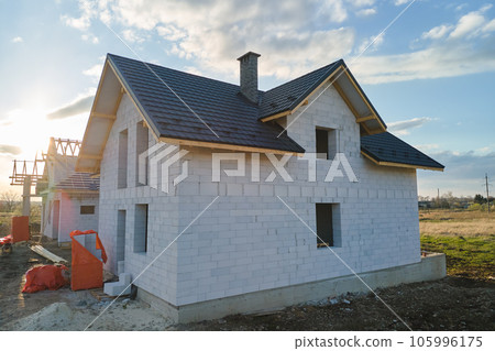 Aerial view of unfinished house with aerated lightweight concrete walls and wooden roof frame covered with metallic tiles under construction. Aerial view of unfinished house with aerated lightweight concrete walls and wooden roof frame covered with metallic tiles under construction. 105996175