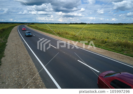 Aerial view of intercity road between green agricultural fields with fast driving cars. Top view from drone of highway traffic 105997296