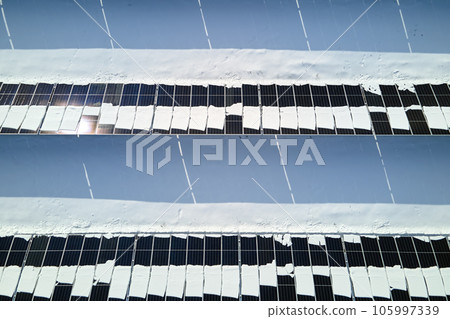 Aerial view of electrical power plant with solar panels covered with snow melting down in winter end for producing clean energy. Concept of low effectivity of renewable electricity in northern region 105997339