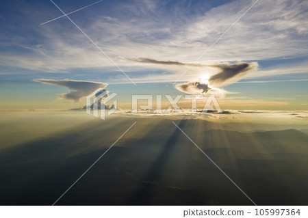 Aerial view of dark mountain hills with bright sunrays of setting sun at sunset. Hazy peaks and misty valleys in evening 105997364