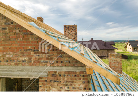 Aerial view of a brick house with wooden roof frame under construction. 105997662