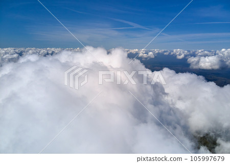 Aerial view from airplane window at high altitude of earth covered with puffy cumulus clouds forming before rainstorm. 105997679