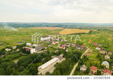 Aerial landscape view of village houses and distant green cultivated agricultural fields with growing crops on bright summer day 105997694
