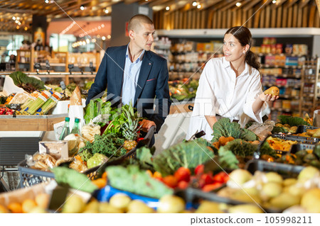 Positive young couple with a grocery cart in the supermarket, choose pears 105998211