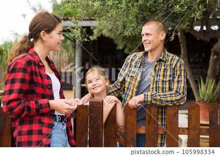 Man, woman and girl talking near fence Man, woman and girl talking near fence 105998334