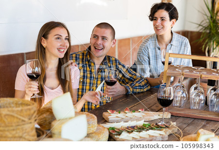 Company of friends tasting cheese and drinking wine while spending time together in winery, indoors 105998343