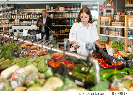 Young girl with a grocery cart selects fresh vegetables in the supermarket 105998383