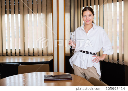 Successful businesswoman with glass of champagne in modern office 105998414