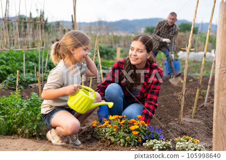 Positive child with her mother caring for flowers at a garden 105998640