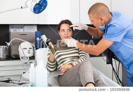 Cosmetologist examining female client face before procedure Cosmetologist examining female client face before procedure 105998696