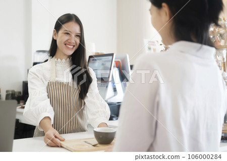 Smiling friendly barista serving  a cup of coffe to customer at coffee shop. 106000284