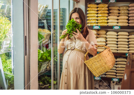 A glowing pregnant woman after forty makes a healthy choice as she selects organic vegetables and fruits at the vibrant organic market, prioritizing her well-being and her baby's health 106000373