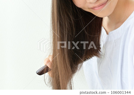 Young woman smiling and taking care of her hair with a brush 106001344