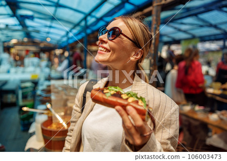 Stylish mature woman is having a takeaway fast food lunch on food market and looking at side Stylish mature woman is having a takeaway fast food lunch on food market and looking at side 106003473