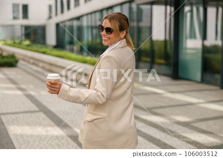 Back view of business woman with coffee walking on modern building background during break time 106003512