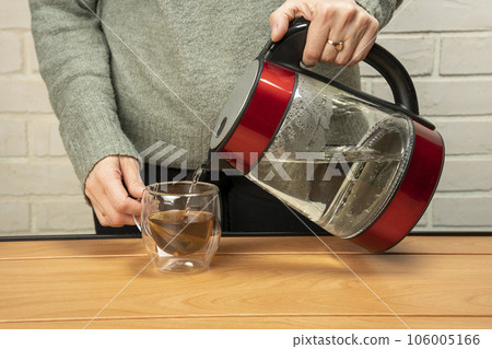 woman pouring hot water from a kettle into a clear glass mug 106005166