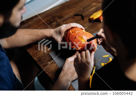 Jack's Halloween pumpkin. Man and child carving face with paper knife. 106005442