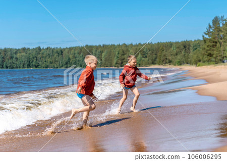 cute caucasian boys wearing red hoodies and blue underpants running from waves in Ladoga lake with enthusiasm cute caucasian boys wearing red hoodies and blue underpants running from waves in Ladoga lake with enthusiasm 106006295