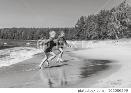 cute caucasian boys wearing red hoodies and blue underpants running from waves in lake with enthusiasm. 106006299