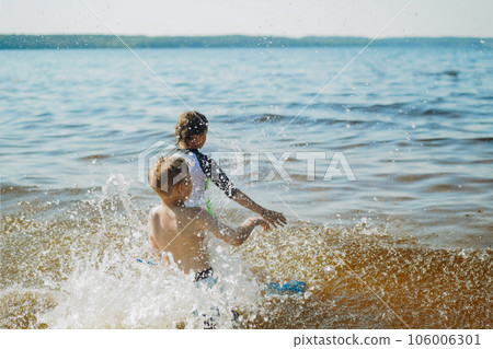 cute caucasian boys running into water with splashes and laughter. Vacatiom on sea side. Happy childhood. Image with selective focus cute caucasian boys running into water with splashes and laughter. Vacatiom on sea side. Happy childhood. Image with selective focus 106006301