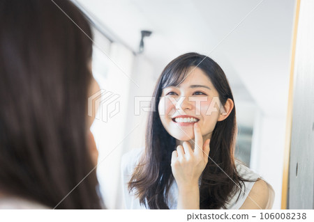 一個 20 多歲和 30 多歲的女人，在鏡子前看著自己的牙齒微笑 106008238