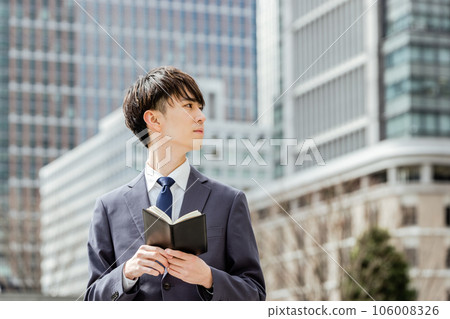 在高樓林立的商圈裡，一名二十多歲的西裝男子，一臉嚴肅地打開筆記本，眺望遠方 106008326