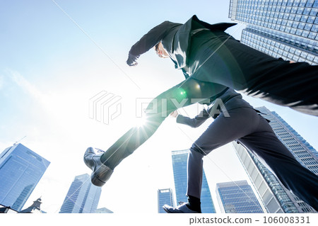 Two business men in suits jumping through a city surrounded by buildings under the blue sky Two business men in suits jumping through a city surrounded by buildings under the blue sky 106008331