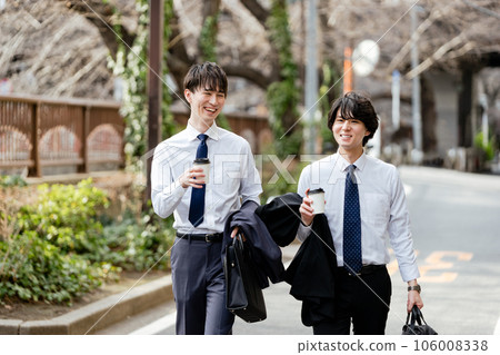 Two young businessmen walking with takeout cups while having a conversation Two young businessmen walking with takeout cups while having a conversation 106008338