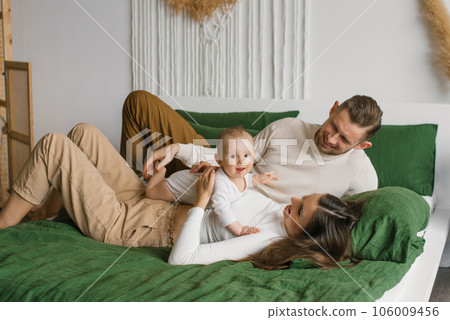 Mother and father are lying on the bed with their little son at home 106009456