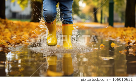 Children's feet in yellow rubber boots walk through a puddle. 106010631