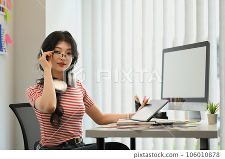 Young stylish female entrepreneur having some creative work, using digital tablet at cozy workplace. 106010878
