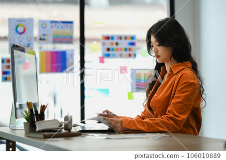 Charming young stylish woman in orange jacket working with color swatch samples chart at office. 106010889