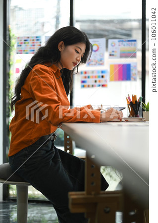 Concentrated young creative woman sitting in bright office and working on design project. Concentrated young creative woman sitting in bright office and working on design project. 106011042