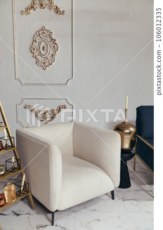 Close up shot of beige soft chair in classic style. Metal candlestick with candles in living room with elegant interior design Close up shot of beige soft chair in classic style. Metal candlestick with candles in living room with elegant interior design 106012335