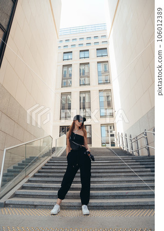Young fashioanable caucasian woman in a black sporty clothes, sunglasses with leather waist bag fanny pack. Street fashion 106012389