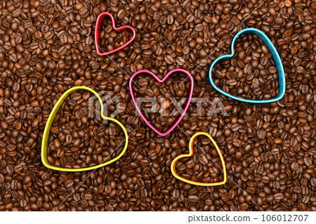 Multicolored hearts in roasted coffee beans background top view. Multicolored hearts in roasted coffee beans background top view. 106012707
