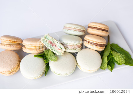 Macaroons of different colors with sprigs of mint on a white background. 106012954