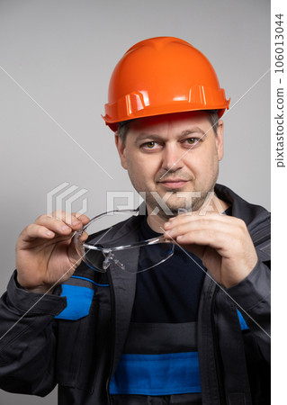 A construction worker in a helmet and overalls put on goggles protective glasses on a white background. 106013044