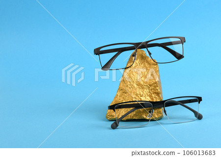 Pair of reading glasses on shining golden nuggets isolated on blue background Pair of reading glasses on shining golden nuggets isolated on blue background 106013683