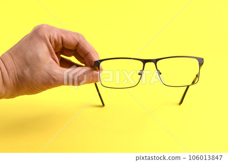 Hand holding plastic black glasses, isolated on yellow background. Hand holding plastic black glasses, isolated on yellow background. 106013847