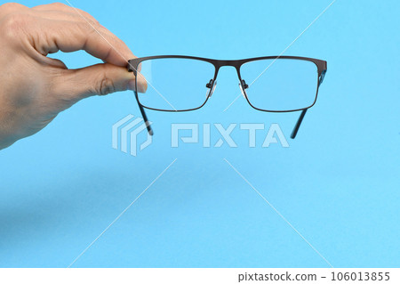 Hand holding plastic black glasses, isolated on blue background. Hand holding plastic black glasses, isolated on blue background. 106013855