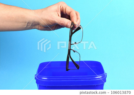 Hand holding plastic black glasses puts in blue container, isolated on white background. Hand holding plastic black glasses puts in blue container, isolated on white background. 106013870