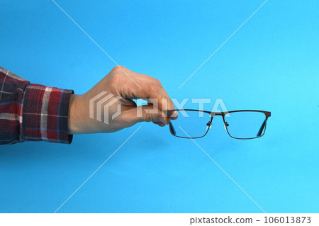 Hand holding plastic black glasses, isolated on blue background. 106013873