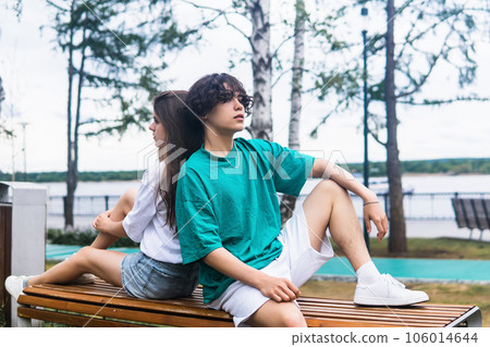 two young people are sitting on a bench in park 106014644