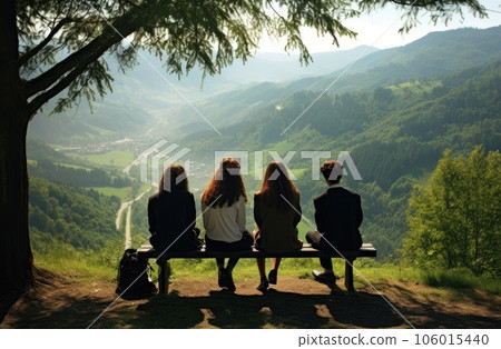 Back view of youth sitting on a bench in the mountains and looking at the valley 106015440